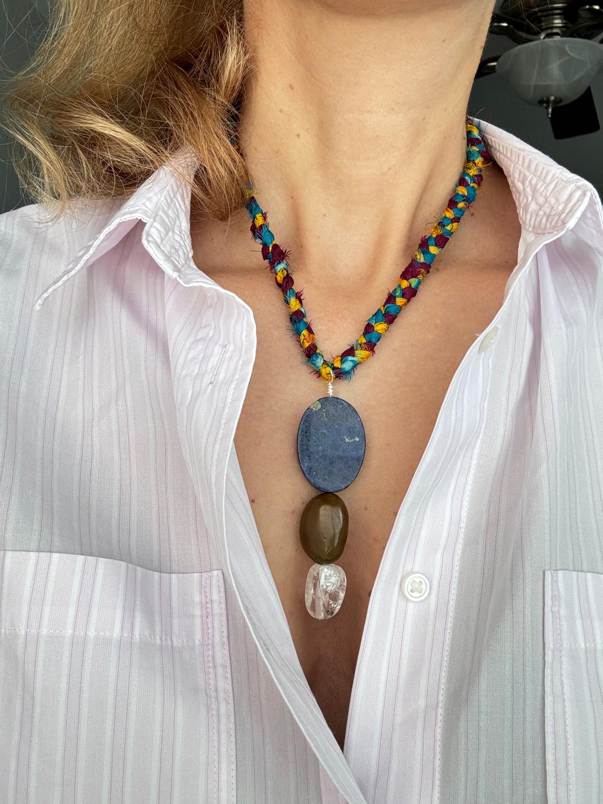 The braided sari silk cord worn at the collarbone, pendant hanging over a white striped shirt