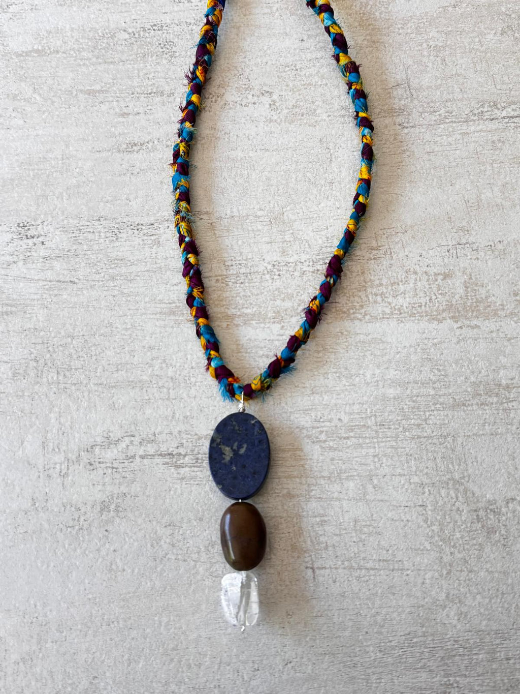 Close view of the stacked pendant: a flat navy lapis lazuli oval, a smooth brown turquoise pebble and a clear crackled quartz nugget