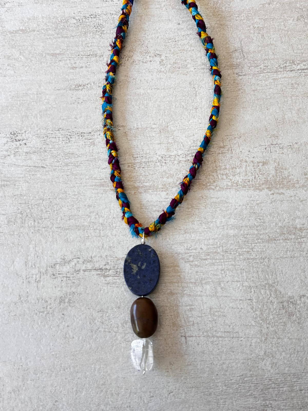 Close view of the stacked pendant: a flat navy lapis lazuli oval, a smooth brown turquoise pebble and a clear crackled quartz nugget