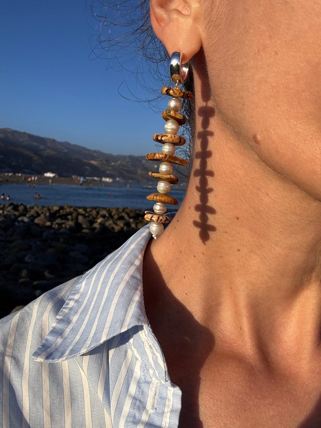 The earrings worn at the beach, the column of pearls and magnesite falling from the ear towards the collarbone