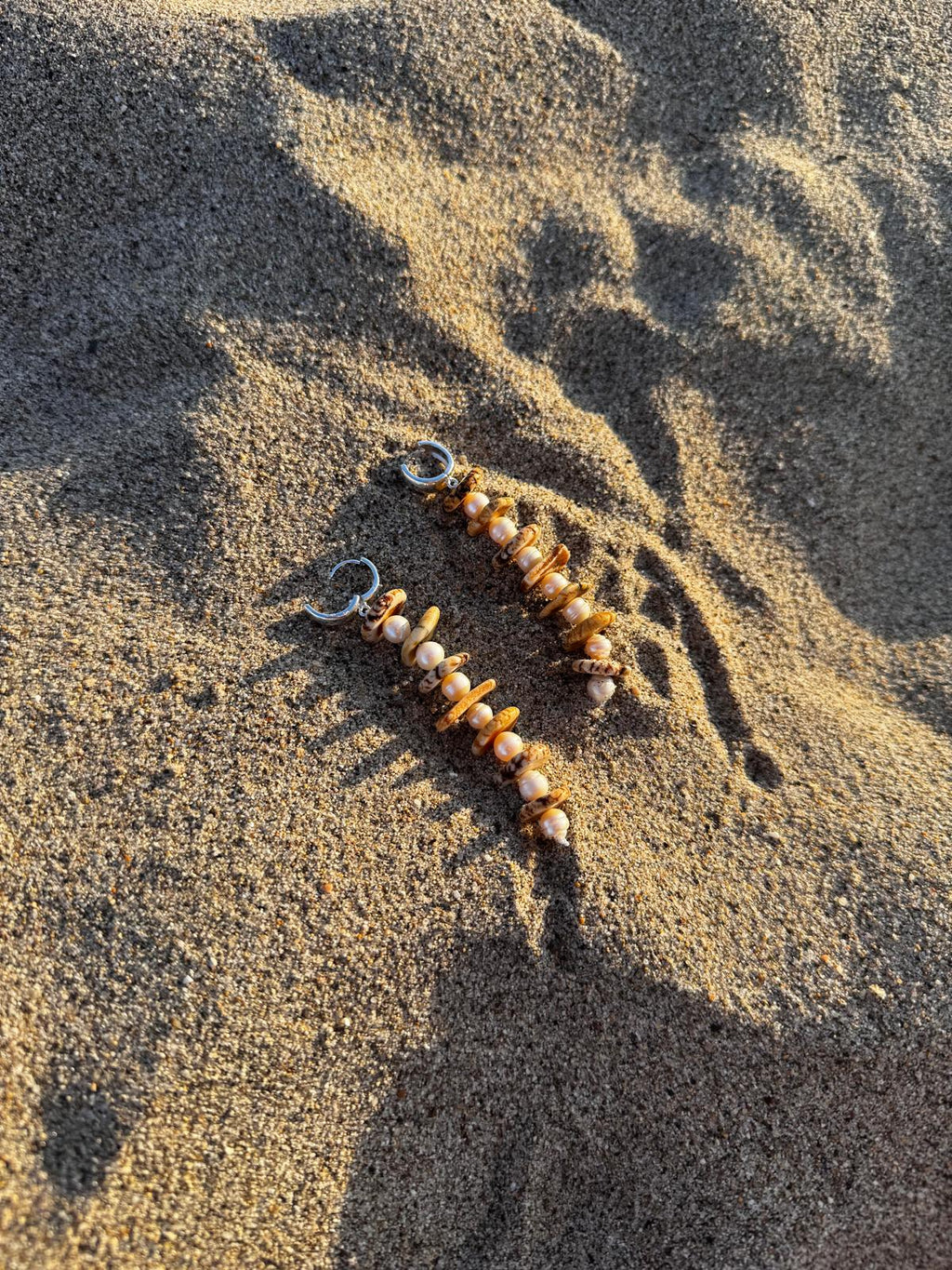Both earrings on sand in low afternoon light, showing the full length of the drop