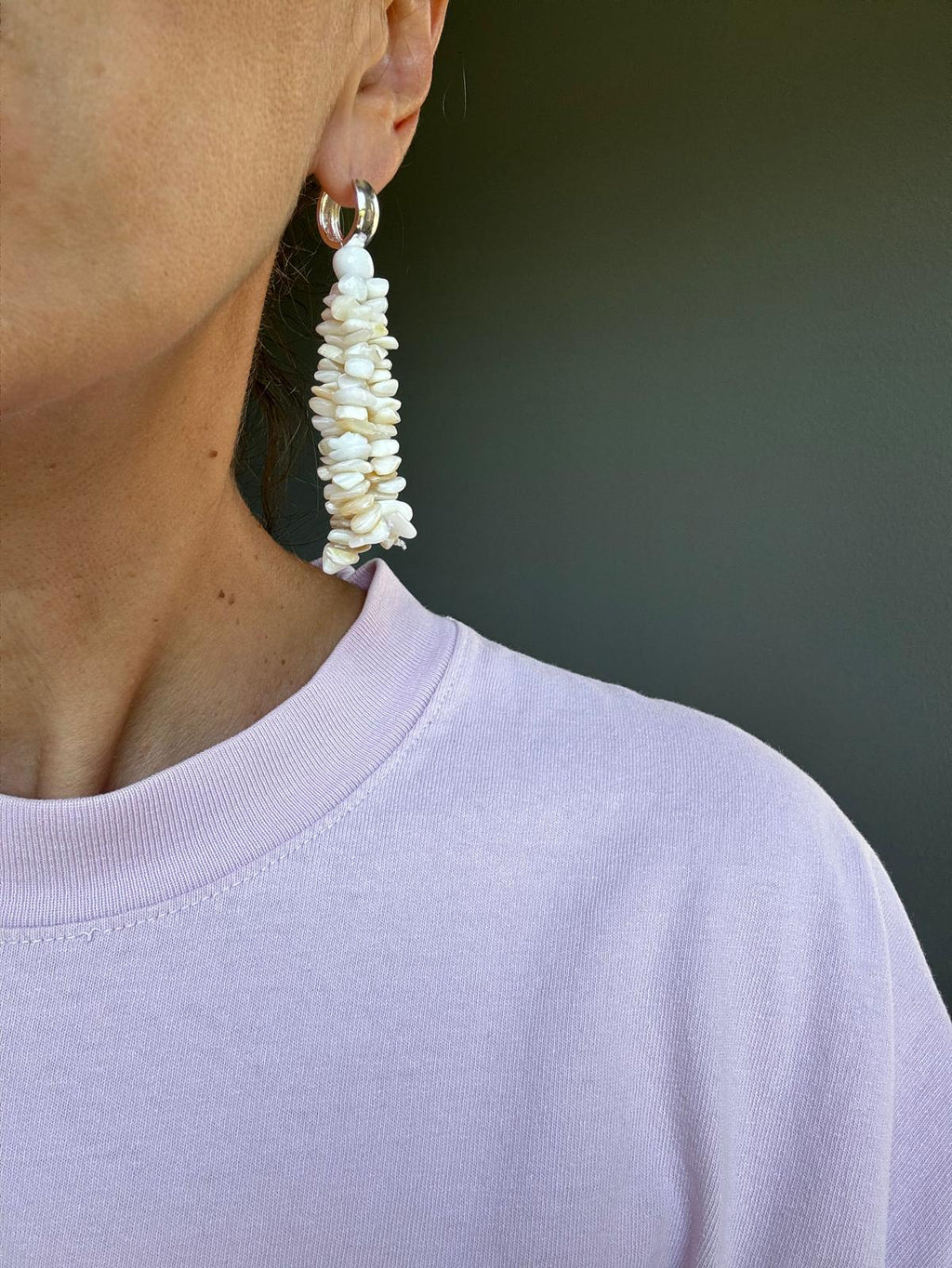 The earring worn, the mother-of-pearl tassel falling from the ear to the shoulder of a lilac t-shirt