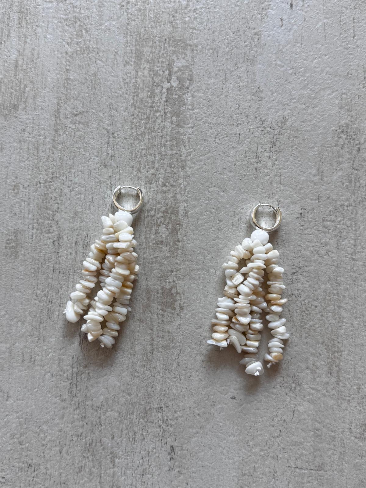 A pair of tassel earrings on pale concrete — strands of cream mother-of-pearl chips hanging from sterling silver huggie hoops