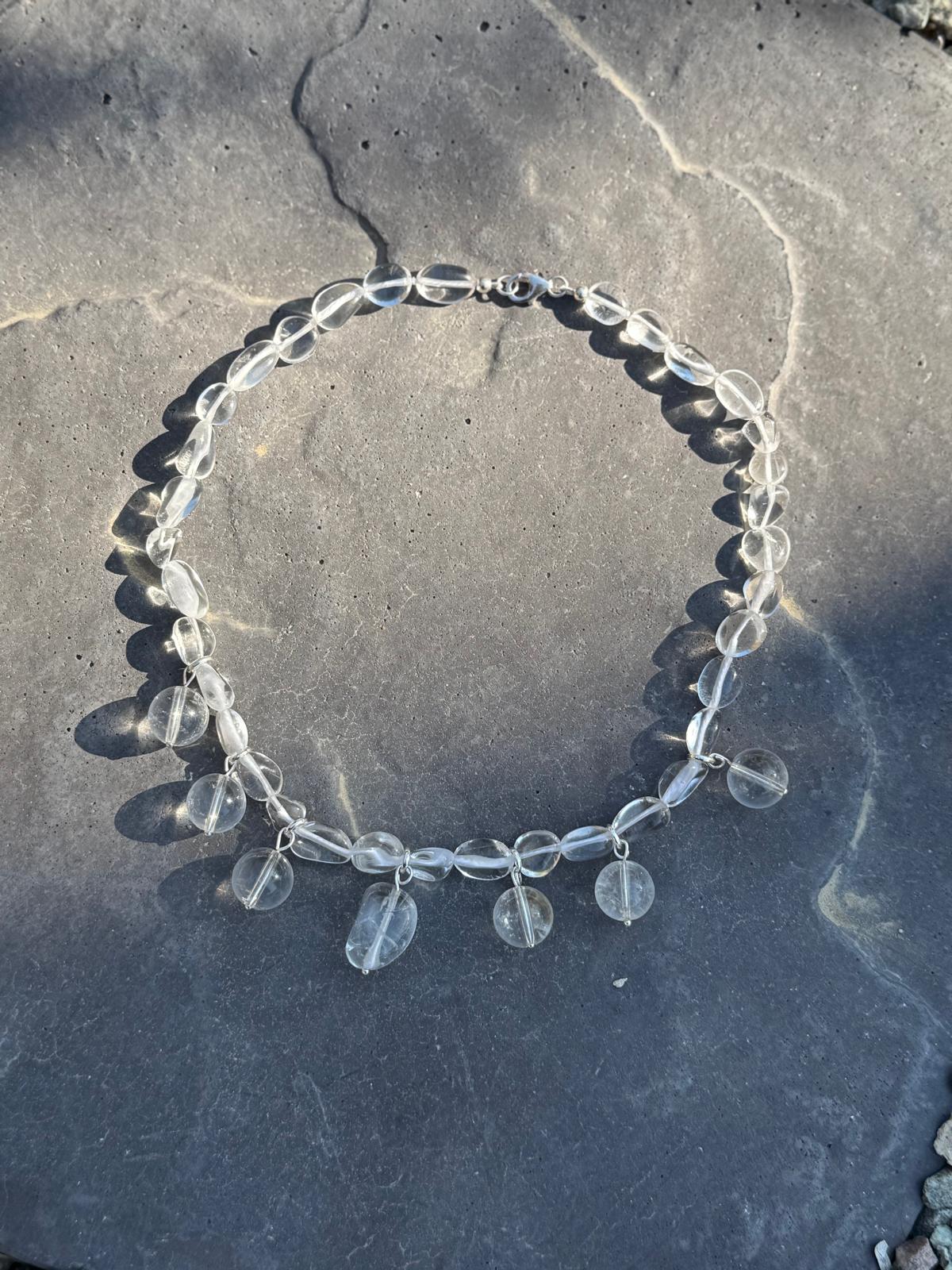 The necklace in sunlight on grey stone, the quartz throwing shadows and catching light