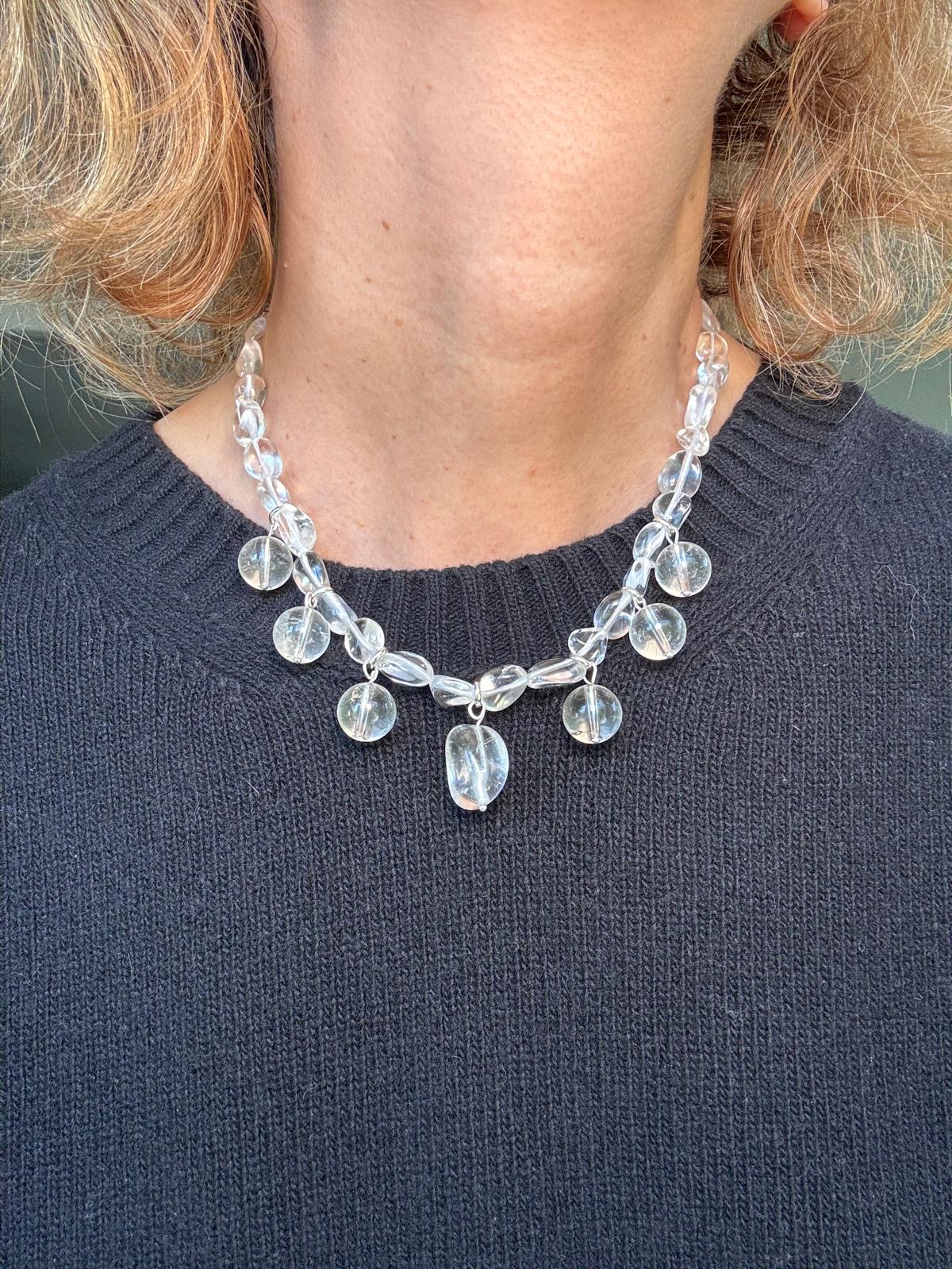 The clear quartz necklace worn over a navy sweater, the drops resting along the collarbone