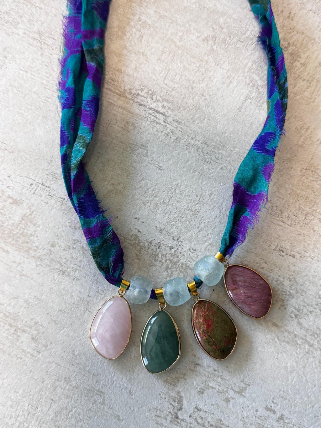 A statement necklace on teal and violet sari silk — four stone cabochons in gold-plated bezels with frosted recycled glass beads between them