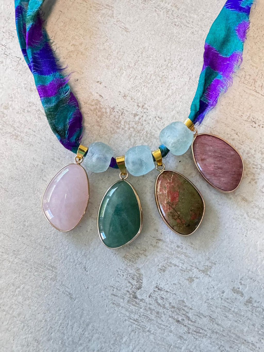 Close view of the four cabochons: rose quartz, green aventurine, unakite and rhodochrosite, with pale aqua glass beads