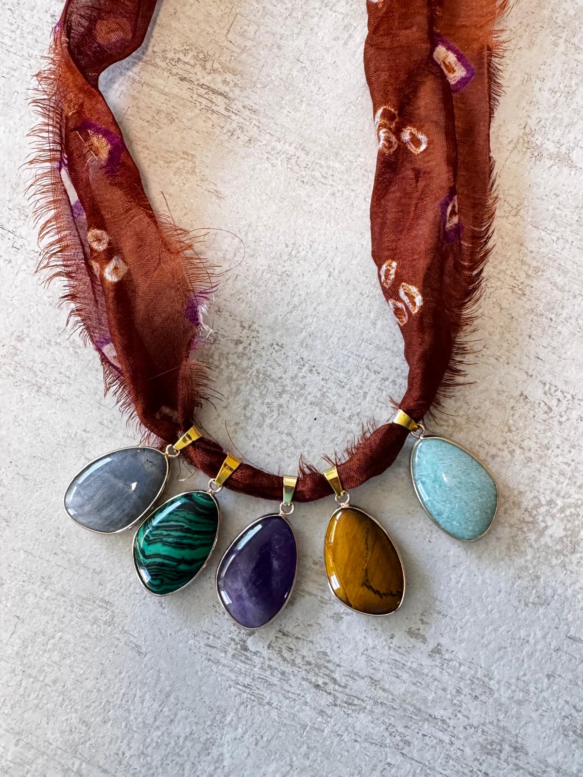 A statement necklace on rust-red shibori-dotted sari silk — five stone cabochons in gold-plated bezels