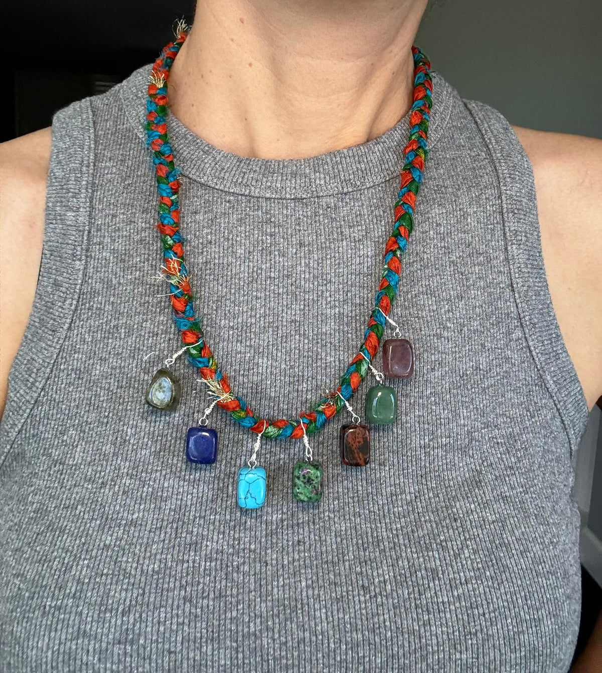 The necklace worn, the tumbled stones in blue, green, red-brown and purple against the braided silk