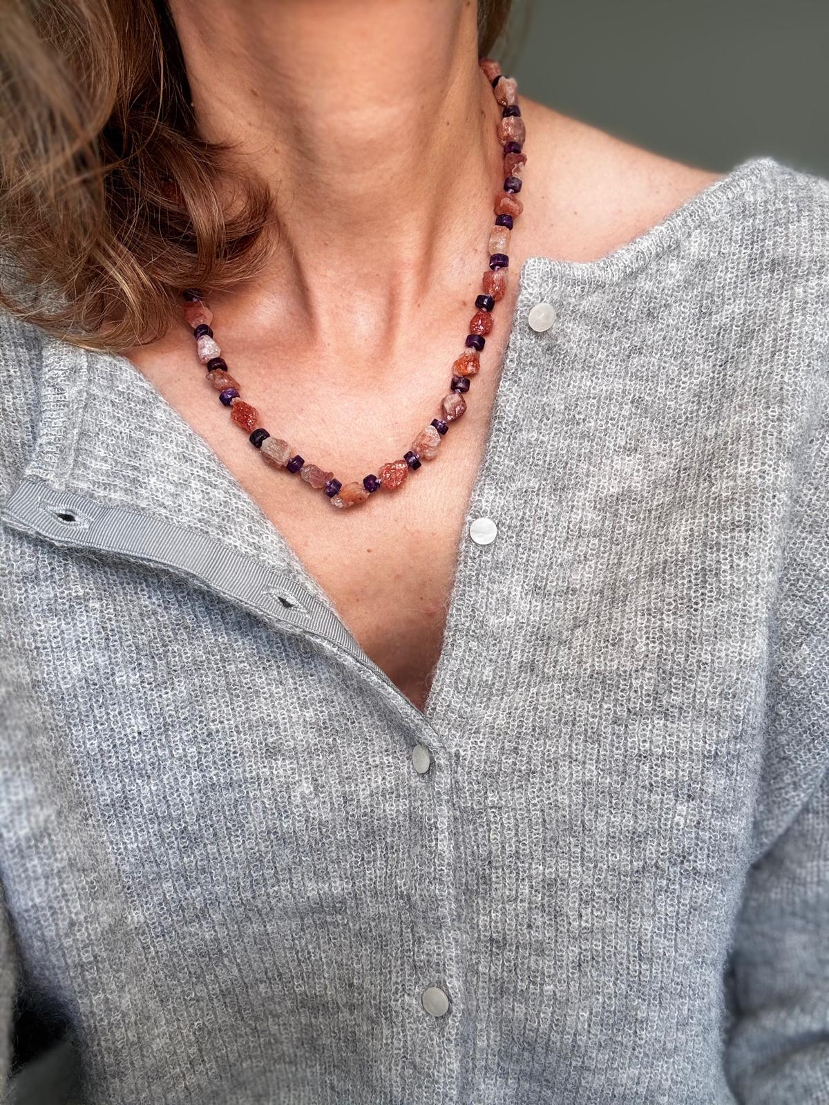The raw sunstone necklace worn over a grey cardigan, orange nuggets spaced with dark purple lepidolite discs