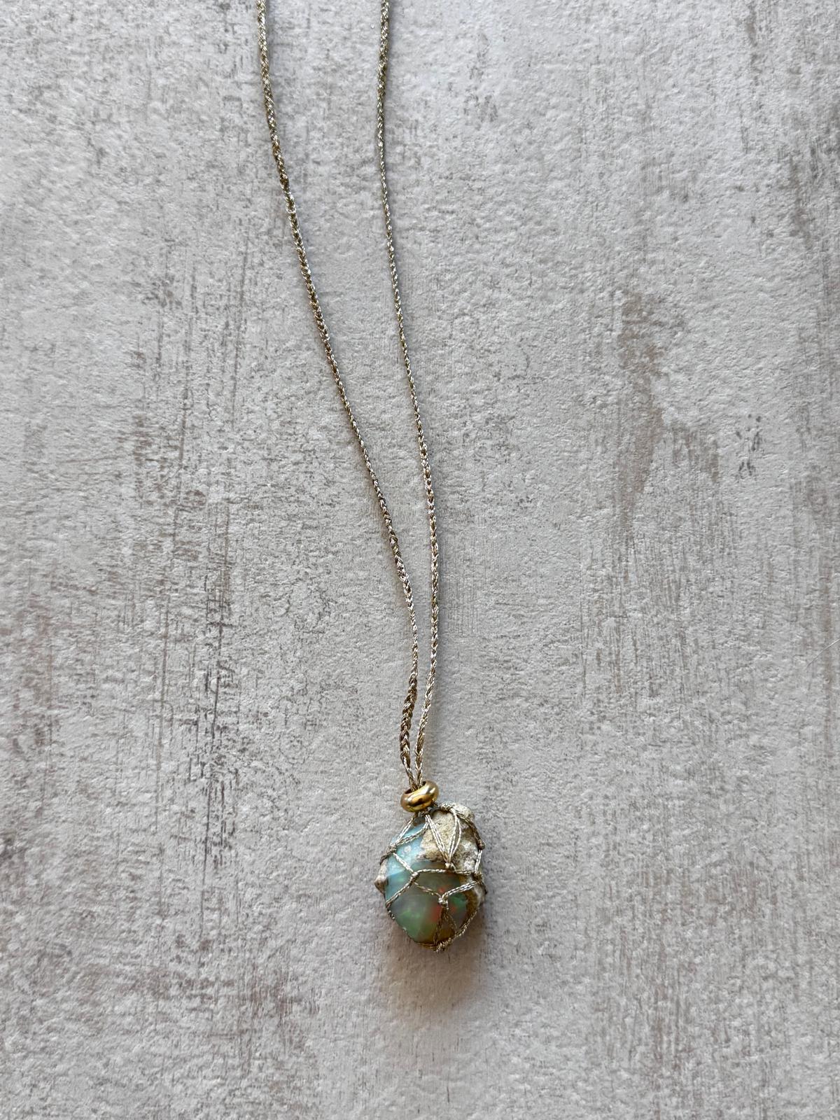 Close up of the unpolished opal held in the braid, with the gold-plated spacer above