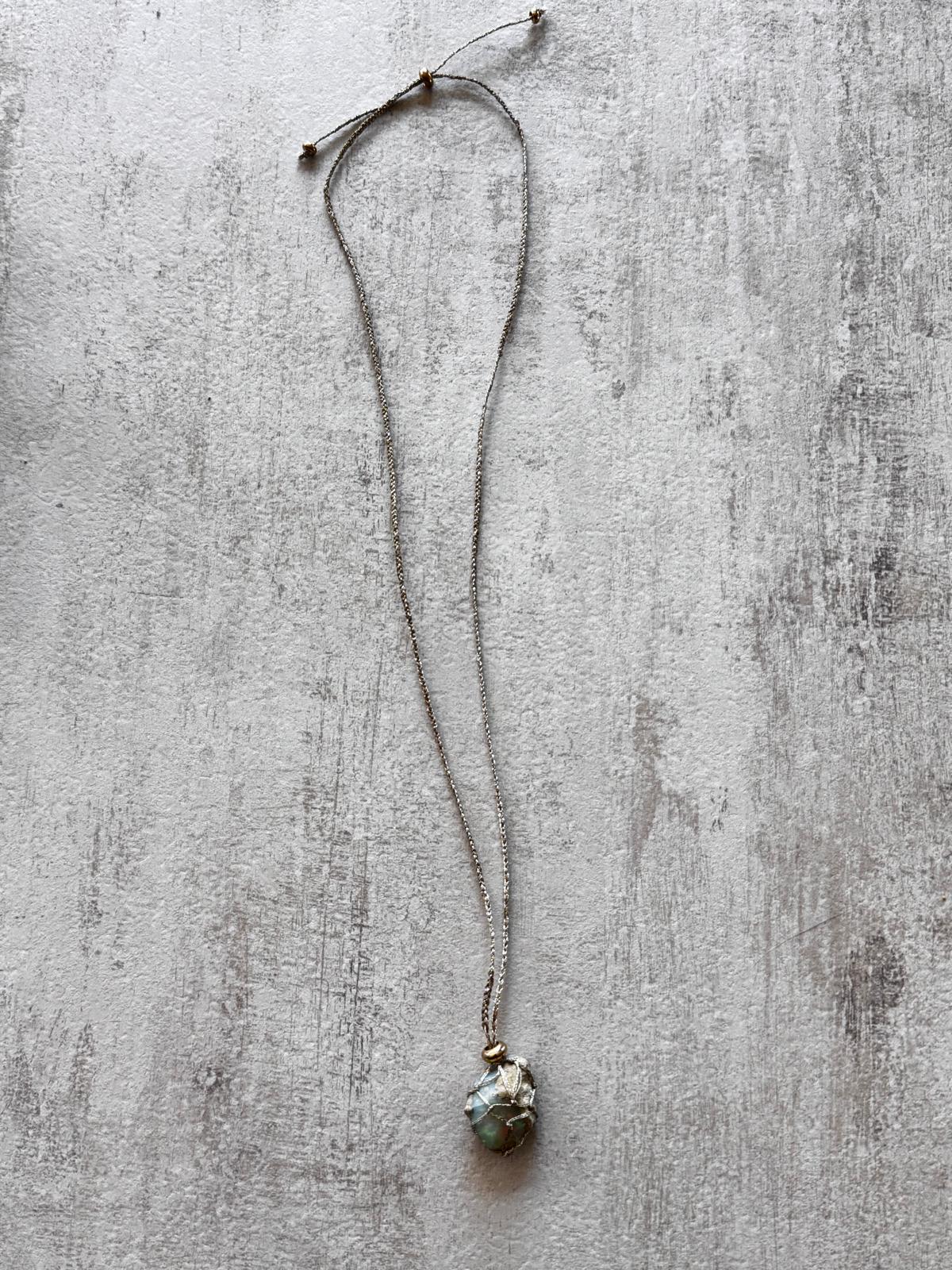 Full view of the raw opal pendant necklace laid flat, adjustable braided cord