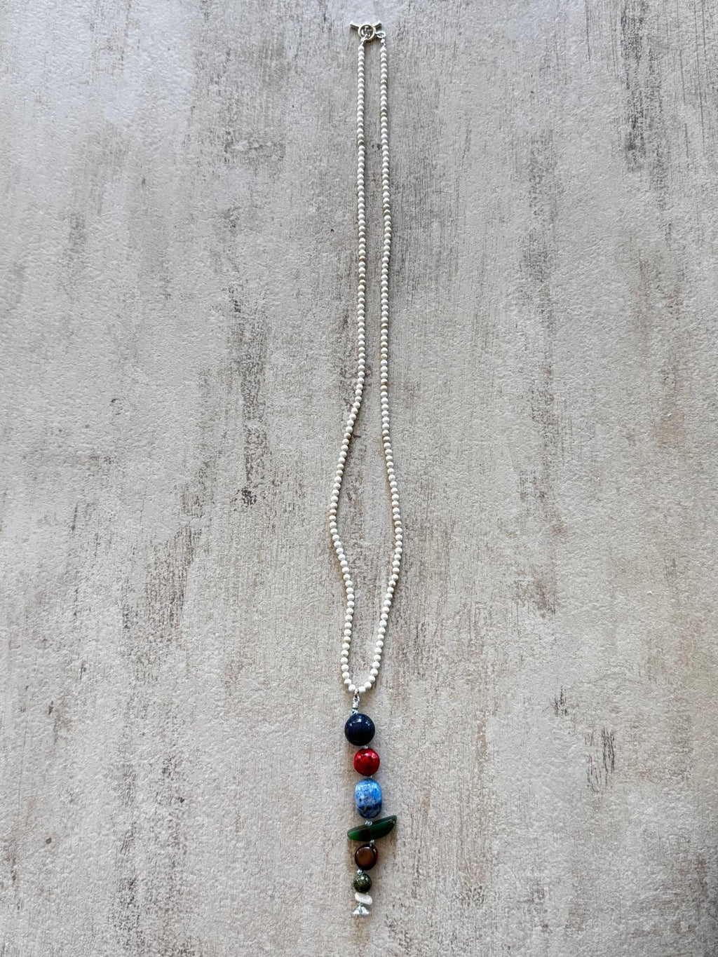 The full necklace laid flat — a fine white howlite strand with a single vertical drop of stacked stones and a sterling toggle clasp