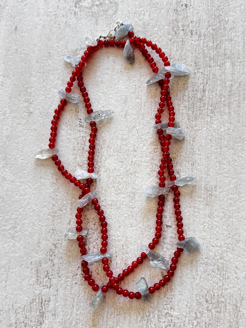 The necklace laid flat and doubled, showing the deep red carnelian rounds and the sterling silver lobster clasp
