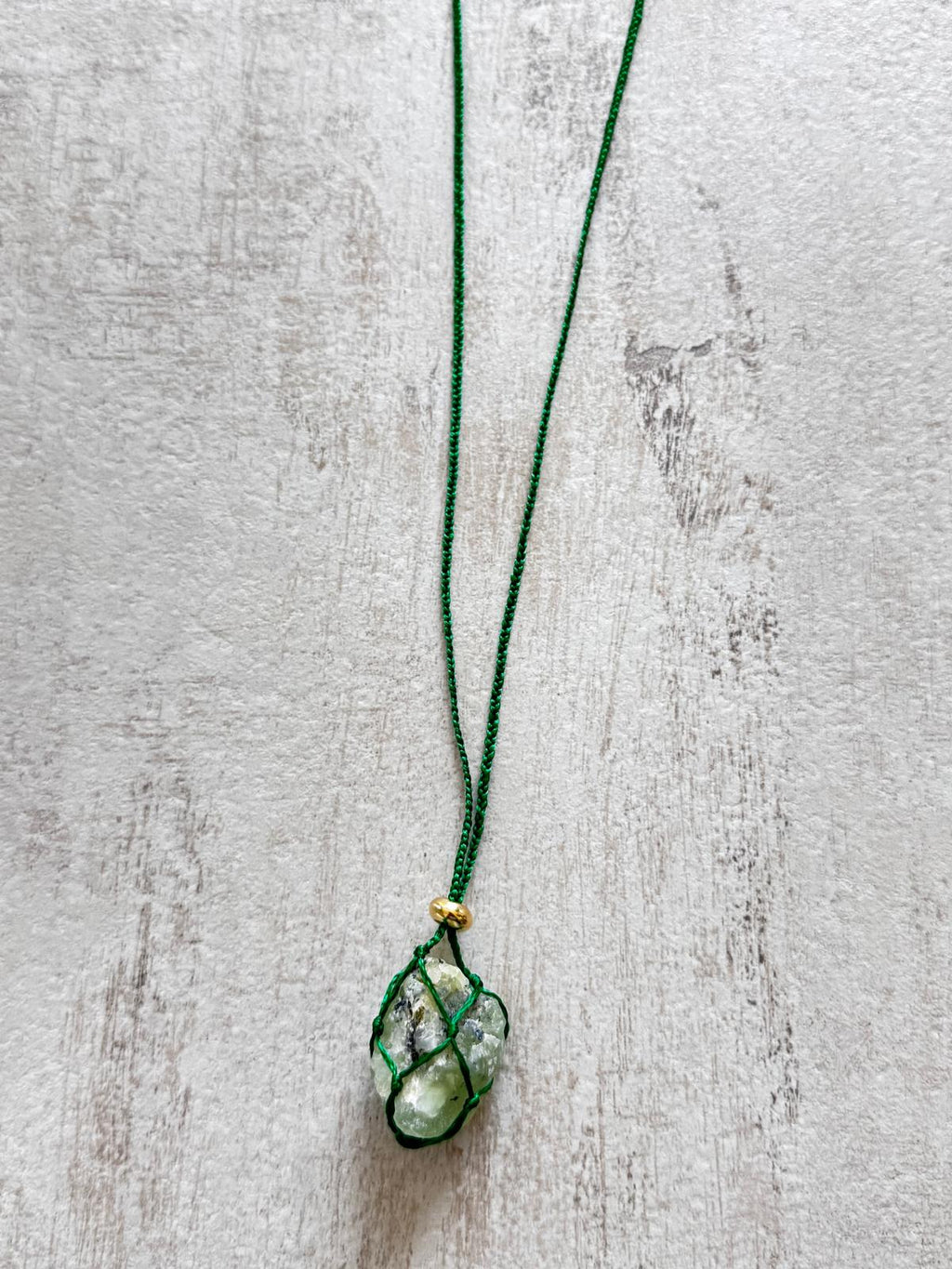 Close up of the raw prehnite pendant held in a green braided net, gold-plated spacer above