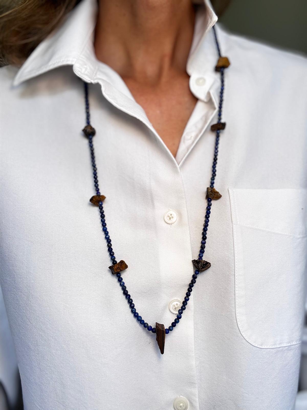 The lapis lazuli and rough tiger's eye necklace worn full length over a white shirt, hanging past the chest