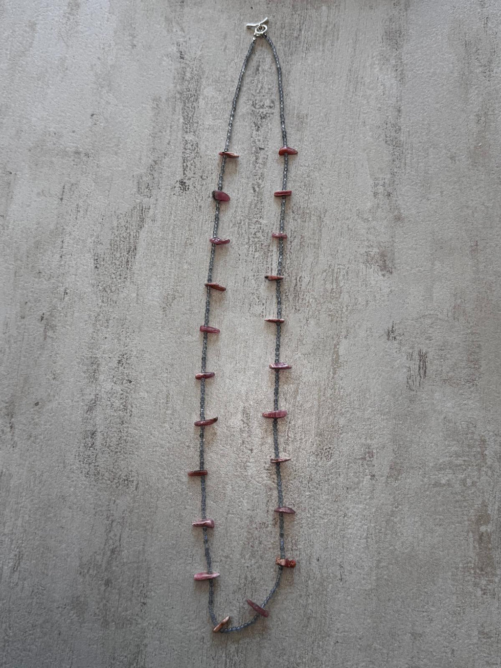 The full length of the necklace laid flat, pink rhodochrosite points evenly spaced along the grey labradorite strand