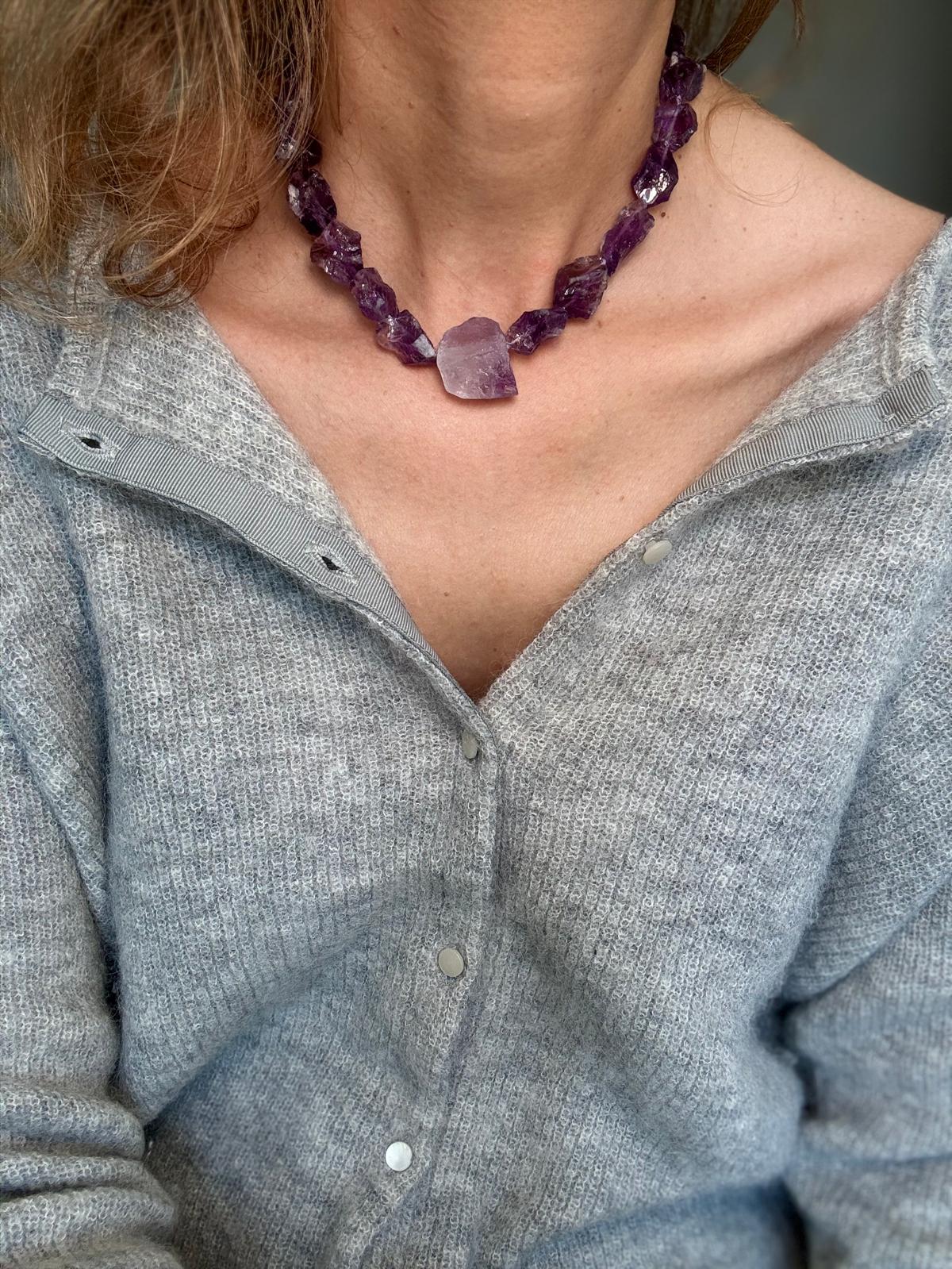 The raw amethyst necklace worn over a grey cardigan, the pale lavender stone sitting at the centre front