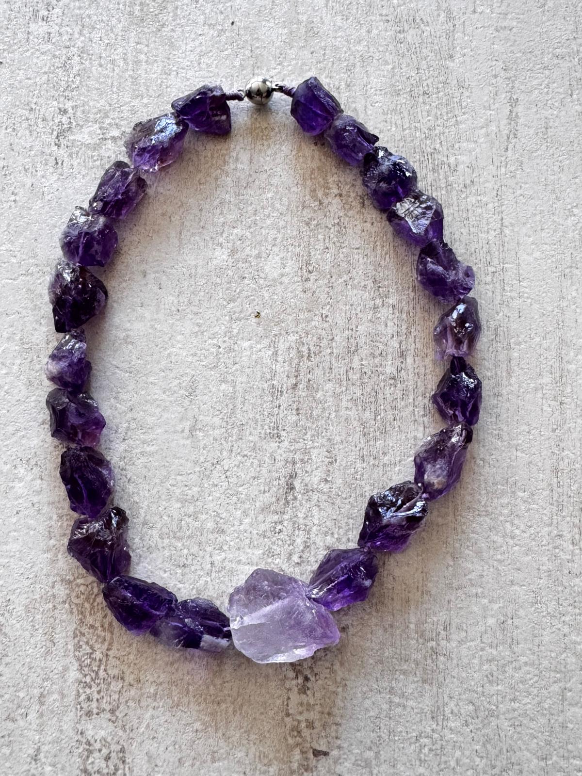 The necklace laid flat — a ring of unpolished deep violet amethyst chunks with one pale stone and a round magnetic clasp