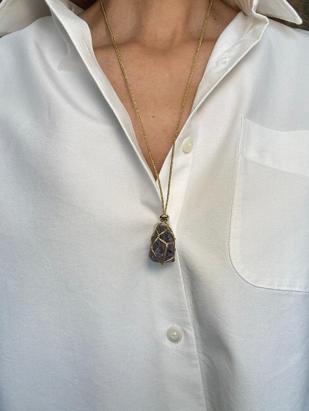 The pendant worn longer on the braided gold cord, hanging at mid-chest