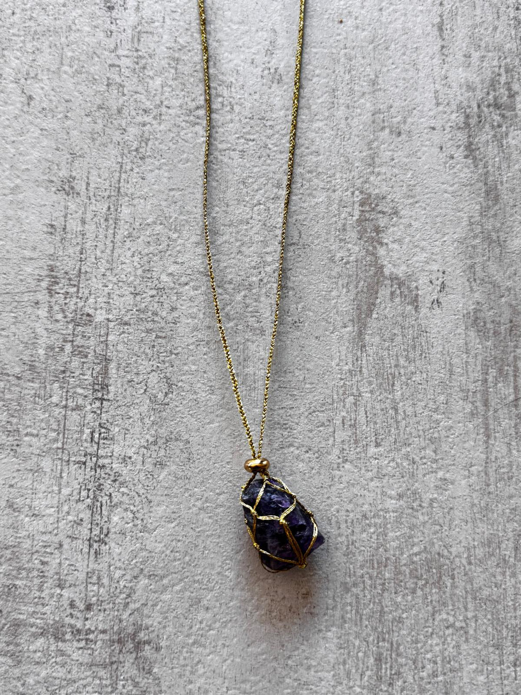 Close view of the dark amethyst caught in the gold braid, with a gold-plated spacer above it