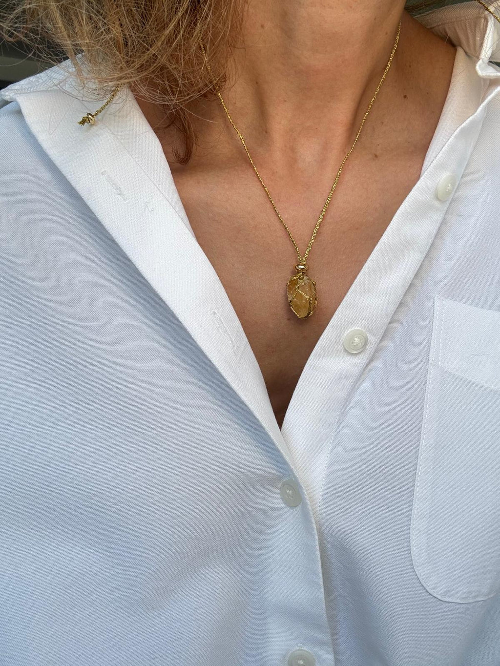 The raw citrine pendant worn over a white shirt, the amber stone held in a hand-braided golden net