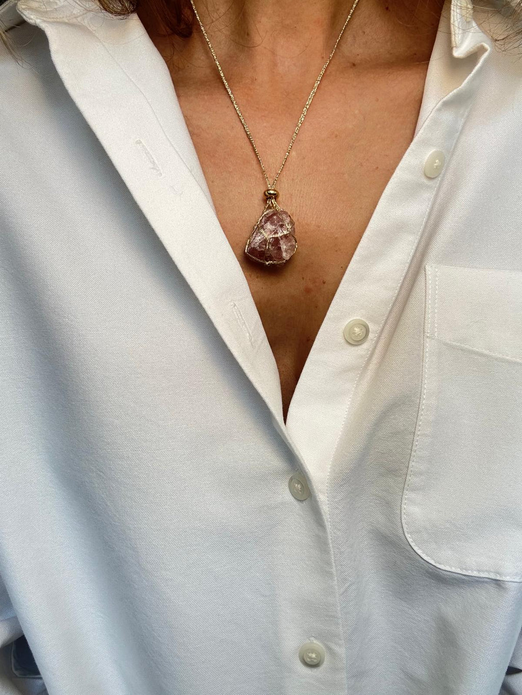 Close view of the pendant, showing the red inclusions inside the pale pink quartz and the gold-plated spacer above
