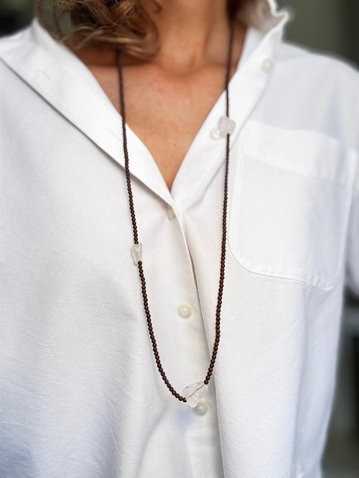The same necklace worn long as a single strand over a white shirt, falling past the chest