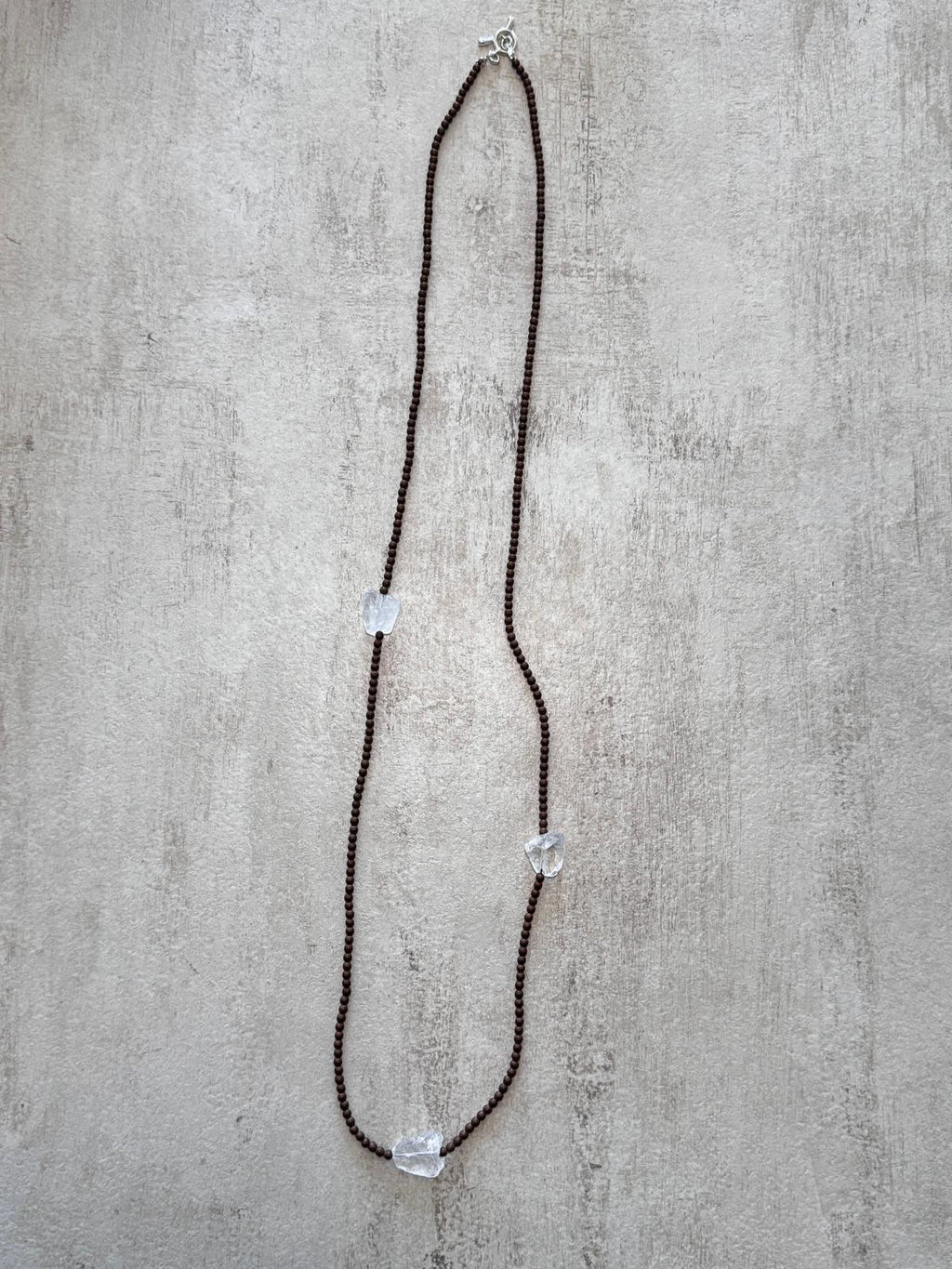 The full length of the necklace laid flat, showing the matte copper hematite strand and the sterling toggle clasp
