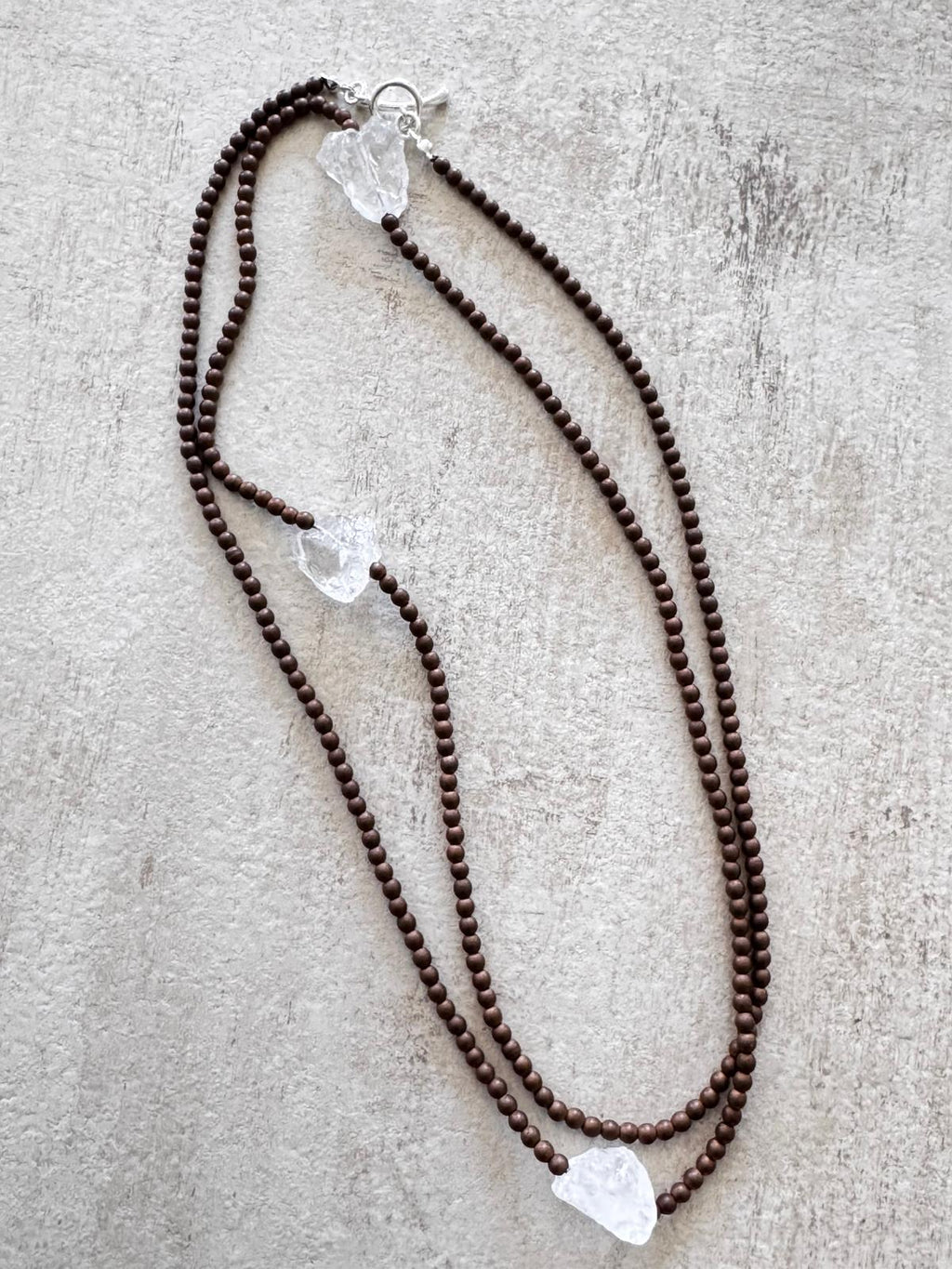 The necklace laid flat and doubled, showing three raw clear quartz nuggets spaced along the strand