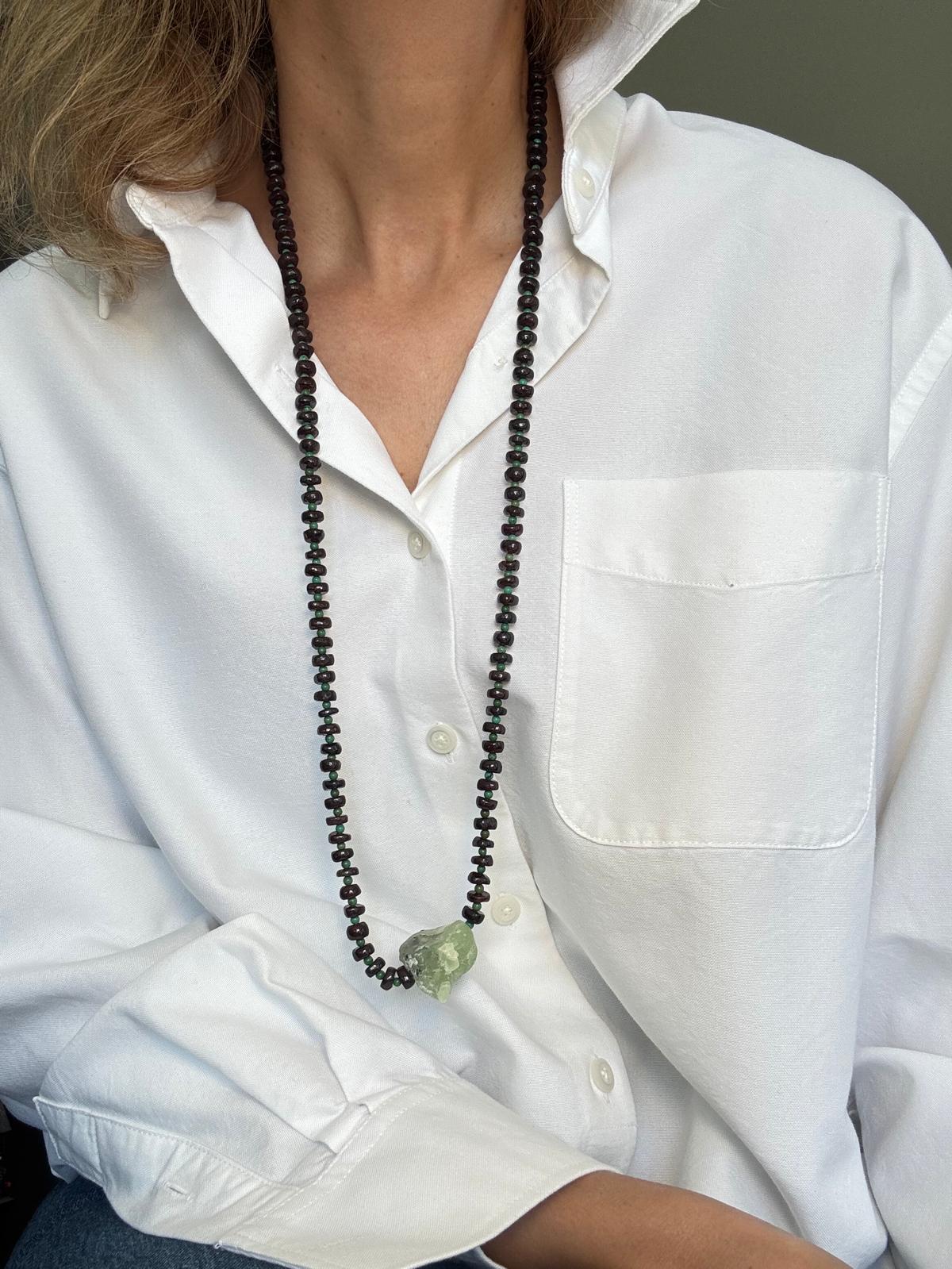 The full length of the necklace worn long, showing the garnet strand and the single raw prehnite