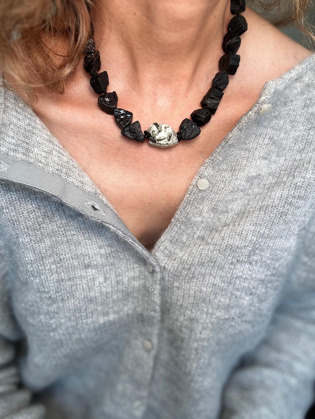 The raw black tourmaline collar worn over a grey cardigan, the pale green prehnite sitting at the centre front