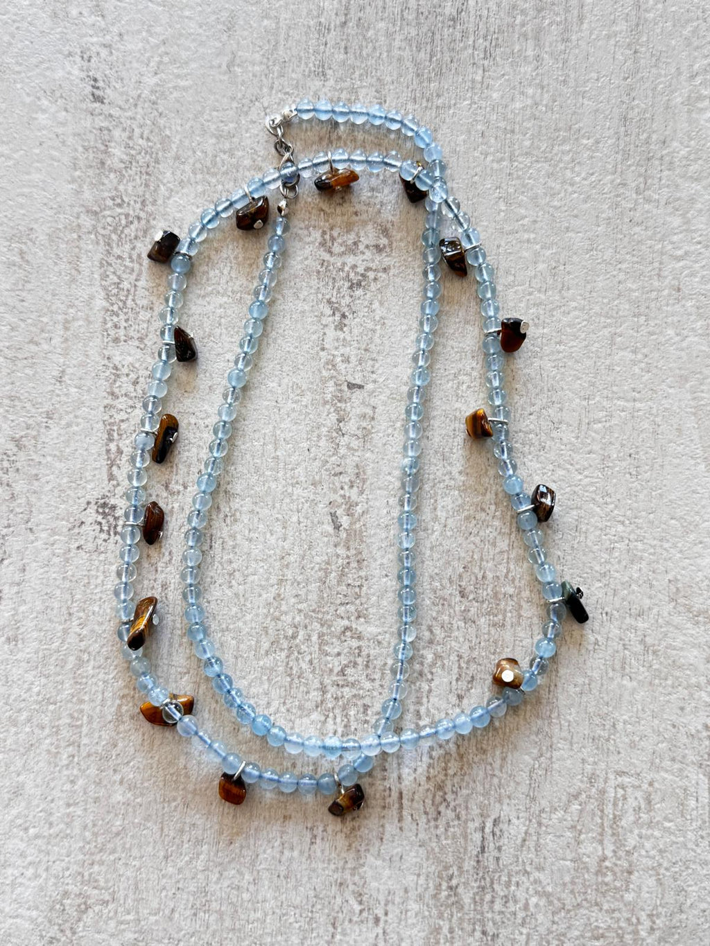 The necklace laid flat and doubled, showing the pale blue aquamarine strand and the brown tiger's eye drops