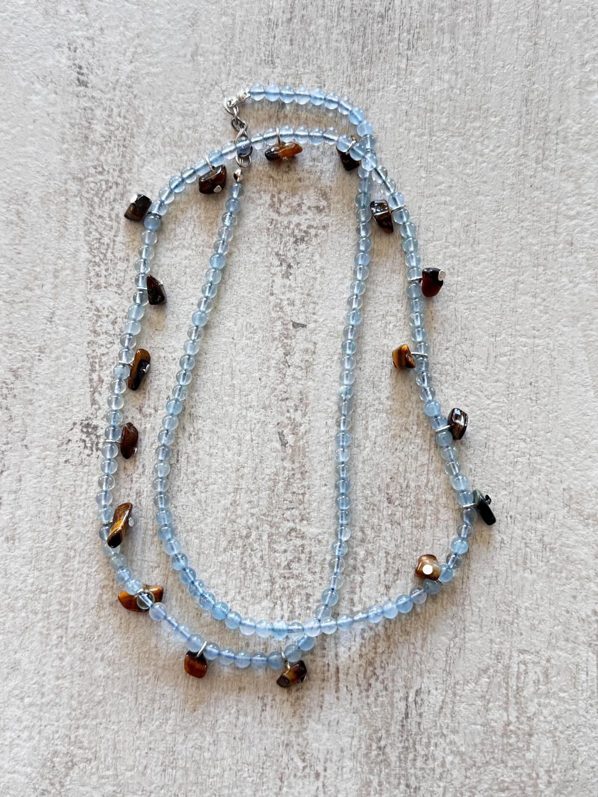 The necklace laid flat and doubled, showing the pale blue aquamarine strand and the brown tiger's eye drops
