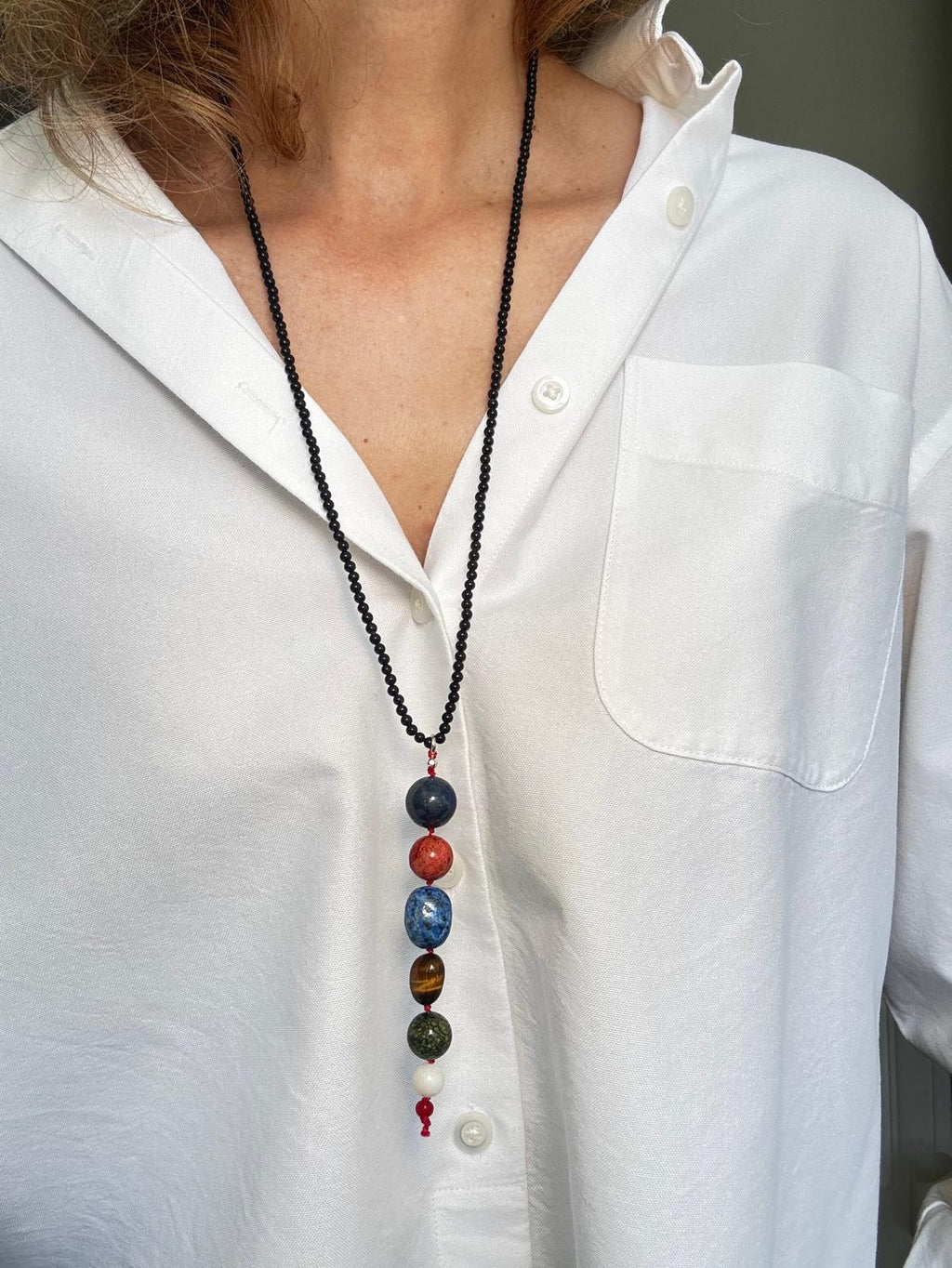 The black onyx necklace worn long over a white shirt, the stacked stone drop hanging at the sternum