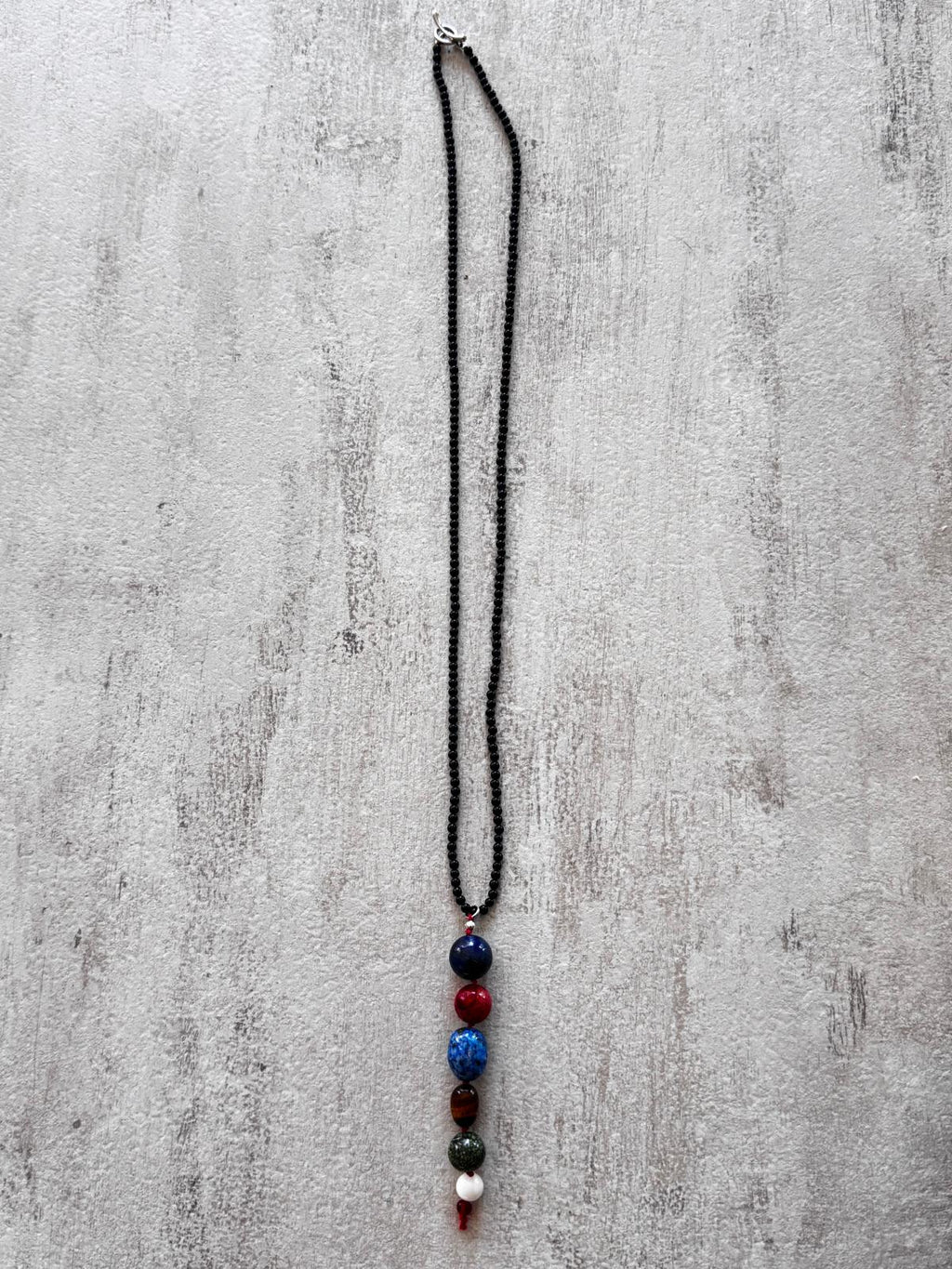 The full necklace laid flat — a fine black onyx strand with a single vertical drop of stacked stones