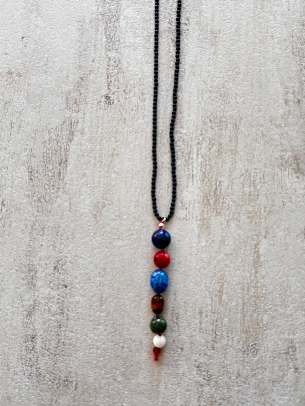Close view of the drop: lapis lazuli, coral, kyanite, tiger's eye, green jasper and mother of pearl stacked in a column, knotted with red