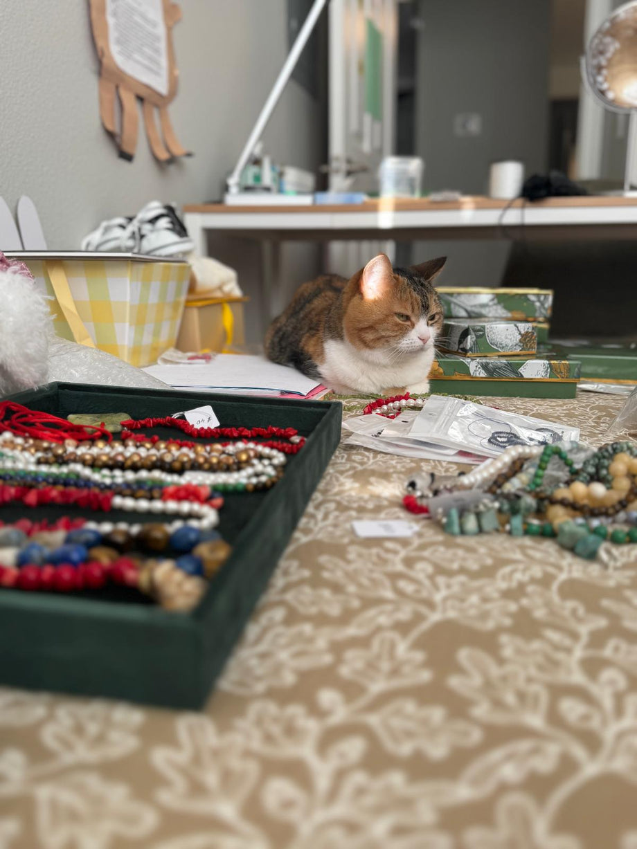 Trays of finished necklaces on the studio table, with the studio cat sitting behind them