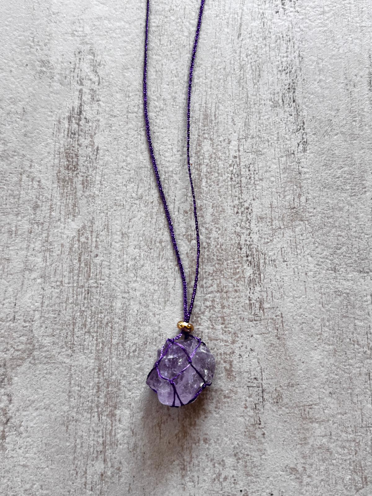Close up of the raw amethyst pendant held in a purple braided net, gold-plated spacer above
